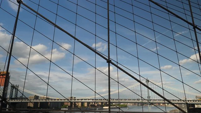 Manhattan Bridge under beautiful spring sky as seen through mesh of Brooklyn Bridge, New York City.