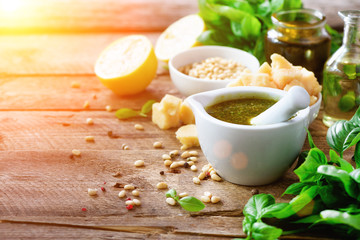 Ingredients for homemade pesto - basil, lemon, parmesan, pine nuts, garlic, olive oil and salt on rustic wooden background. Top view, flat lay, copyspace. Sunny morning