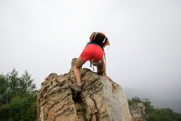 Fototapeta premium successful woman climber climbing rock on the top of mountain