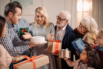 family presenting cake and gifts to woman