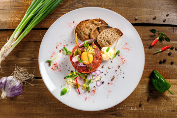 Plate with delicious tartare, toasted bread and salad on a wooden table. Healthy gourmet French food made of raw meat. Top view.