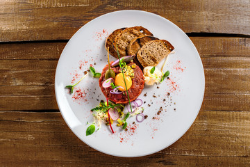 Delicious tartare with toasted bread and salad on a plate. Healthy lunch meal made of raw meat. Classical French cuisine.  Top view.