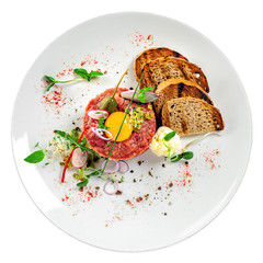 Gourmet tartare, toasted bread and salad on a plate. Delicious healthy French cuisine meal made of raw meat isolated on white background. Top view.