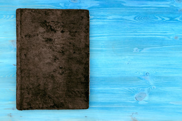 Closed bown vintage book with suede cover isolated on blue wooden table surface background. Education background with copy space.