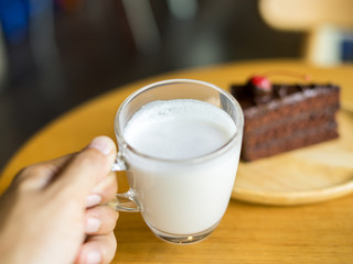 Hand holding glass of milk with chocolate cakes on top red cherry background in wooden plate on wood table