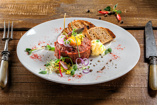 Delicious tartare with toasted bread and salad on a plate. Healthy lunch meal made of raw meat. Classical French cuisine.