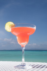 Strawberry Daiquiri cocktail on the white rattan table at the beach restaurant with beautiful blue sea and sky background