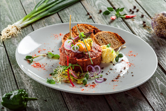 Delicious tartare with toasted bread and salad on a plate. Healthy lunch meal made of raw meat. Classical French cuisine.