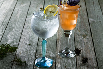 Alcoholic gin and tonic cocktail with drink made of rum, soda, ice and basil leaf in a long glass on a wooden table.