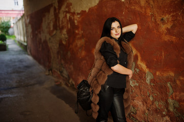 Fototapeta na wymiar Fashion outdoor photo of gorgeous sensual woman with dark hair in elegant clothes and luxurious fur coat at old street with grunge walls.