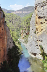 Fototapeta na wymiar Summertime scene of Mijares river between mountains of limestone rocks, in Montanejos (Castellon - Spain). Beautiful turquoise blue waters. Natural landscape. Sunny day with some clouds.