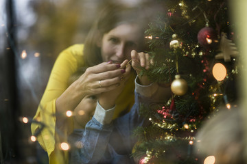 Happy young mother and her toddler son decorating Christmas tree