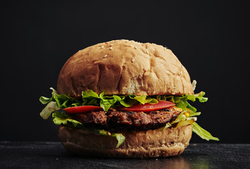 Closeup of tasty beef burger with cheese, lettuce and tomato on dark background. 