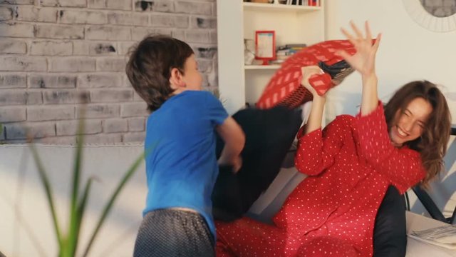 Beautiful mother and child beating pillows playing together bed home smiling feel happy chid family modern design having fun enjoying sitting room sofa casual Slow Motion Shot Shot on RED EPIC camera