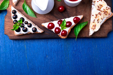 Fruit toast on wooden board on blue rustic background. Healthy breakfast. Clean eating. Dieting concept. Grain bread slices with cream cheese and various fruit, berries, seeds. Vegetarian. Top view.