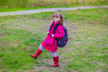 Fototapeta premium Little cute schoolgirl with a big backpack walking on the grass in the autumn day