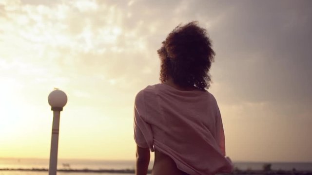 picture of young skinny girl standing from back in front of the sea greeting new day with open arms stretching body during dawn slowmotion