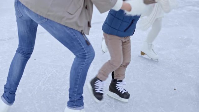 Tilt down of happy couple and cute little children in warm clothing holding hands and ice skating in circle on outdoor rink in winter