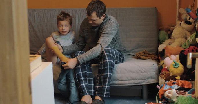 Father getting his son dressed in jeans while kid attracted to the TV