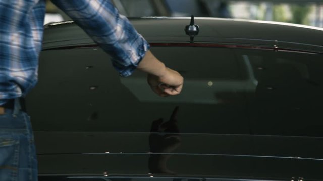 A man traces heart shapes on a car window with his index finger.