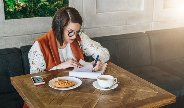 Young businesswoman is sitting in cafe at table,working. Girl fills out an application, questionnaire, signs documents, draws up resume.Student is studying online, doing homework.E-learning,education.