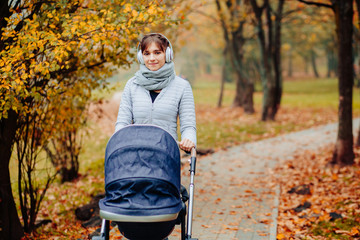 Young sporty mother woman listen to music on headphones and walking with sleeping child in baby...