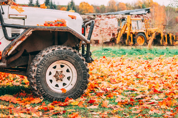 A part of the off-road car parked in the place full of yellow red autumn leaves