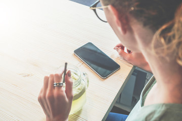 Top view. Close up smartphone with blank screen on table. Hipster girl is sitting in cafe, using phone, looking on his screen,chatting.Young businesswoman working online.Online education.Social media.