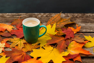 Coffee Cup of cappuccino and autumn leaves on background old dark wood planks.