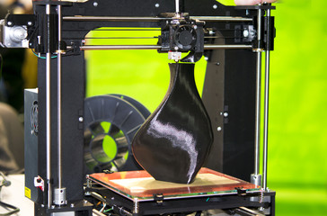 3D printer printing a model in the form of black vase close-up. The concept modern additive...