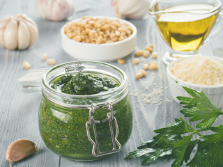 Homemade parsley pesto sauce and ingredients on gray wooden background. Close up wiev of parsley pesto in glass jar with ingredients.