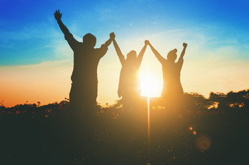Silhouette of happy teamwork hold hands up as a business successful, business victory. Sun len...