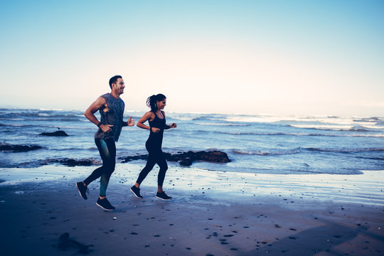 Fit young adult couple running on beach