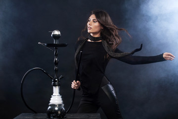 Fototapeta na wymiar Young, beautiful woman in the night club or bar smoke a hookah or shisha. The pleasure of smoking. Sexy smoke.