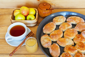 Freshly baked homemade pies on a round baking sheet, a cup of tea, a jar of honey and apples on a wooden table. Rustic Still Life