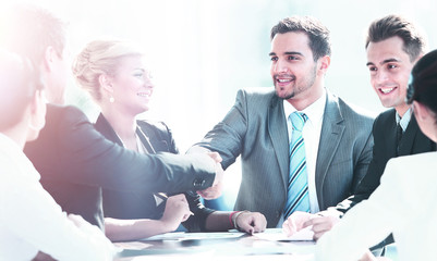 Business colleagues sitting at a table during a meeting with two male executives shaking hands