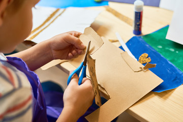 High angle portrait of unrecognizable little boy cutting paper in arts and crafts class of...