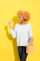 Portrait of a beautiful african woman in blue sweater standing with shopping bag on the yellow background