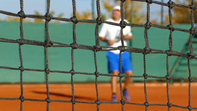 Mature man playing tennis on clay court, net in front