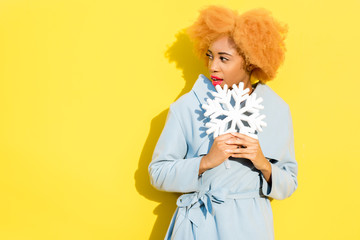 Lifestyle portrait of a beautiful african woman in blue coat with artificial snowflake on the yellow background. Autumn concept