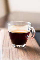 Glass of americano espresso fresh made dark black strong coffee on wooden board table, thick froth foam in cafe, morning refreshing hot drink caffeine, copy space for text