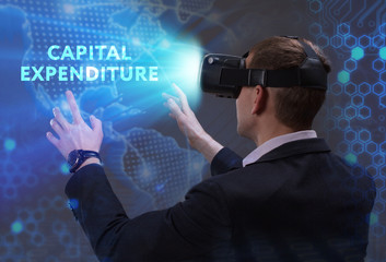 Business, Technology, Internet and network concept. Young businessman working in virtual reality glasses sees the inscription: Capital expenditure