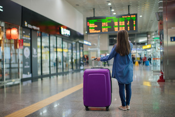 The girl with a suitcase on wheels, standing on a floor in the modern terminal of the airport...