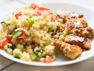 Turkey meat, fried, with teriyaki sauce and sesame seeds. A side dish of Couscous with vegetables. Selective focus, day natural light, side view