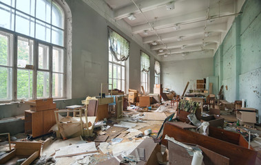 Large room with large vintage windows and broken furniture and trash on the floor. The premise of an old abandoned textile factory