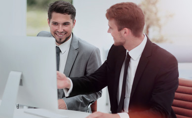 Smiling business men showing something on computer as colleague 