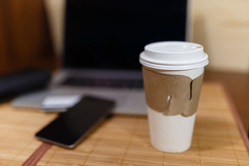  White paper Cup with burning coffee on the background of laptop and smartphone to Work on the go.