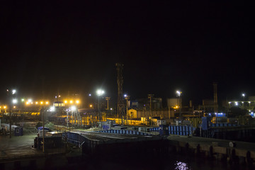 a large sea port on a dark night, you can see cranes and boats