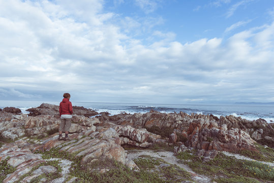 Tourist looking with binocular on the rocky coast line at De Kelders, South Africa, famous for whale watching. Winter season, cloudy and dramatic sky, toned image.