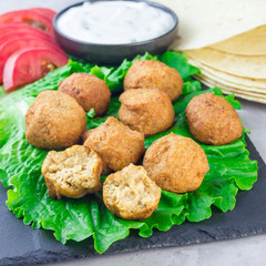Chickpea falafel balls on slate board with vegetables and sauce, square